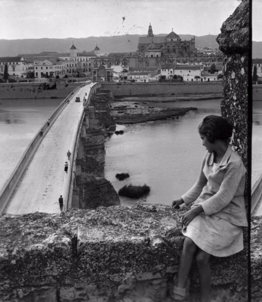 Archivo:Joven mujer en las almenas de la Torre de la Calahorra con puente Romano y pueta del Puente a lo lejos (1931). George Lewis.png